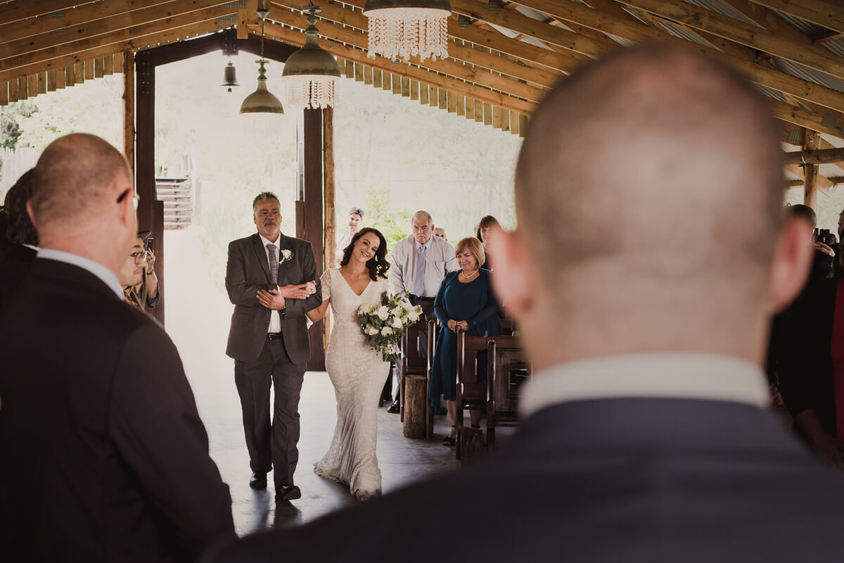 Bride walking down the aisle at the start of wedding ceremony with groom looking on.