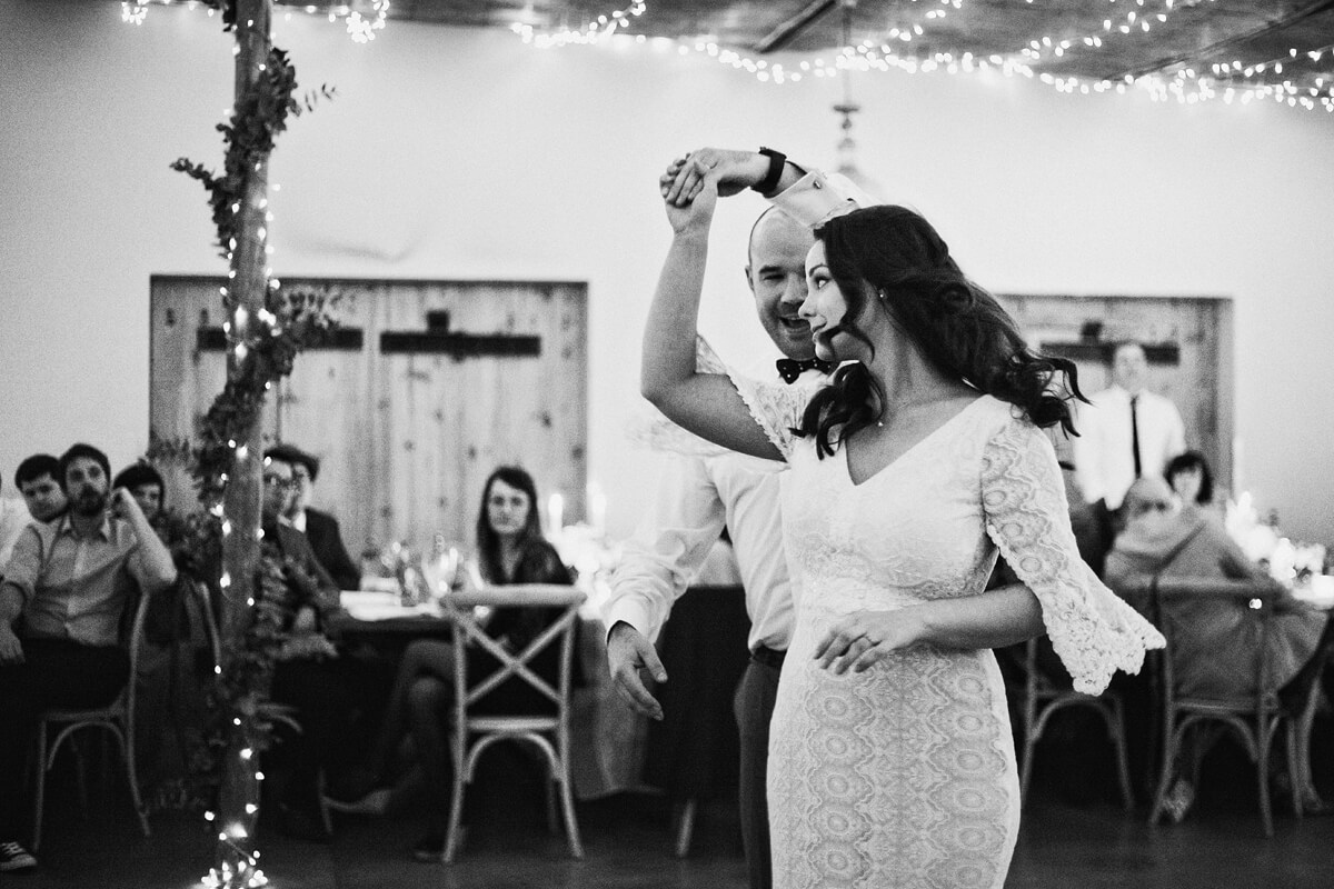 Bride and groom having their first dance as a married couple with guests looking on in the background.