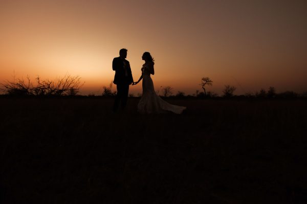 Bride and groom silhouetted in the veld with warm African sunset colours and iconic tree shapes at Ngala Lodge.