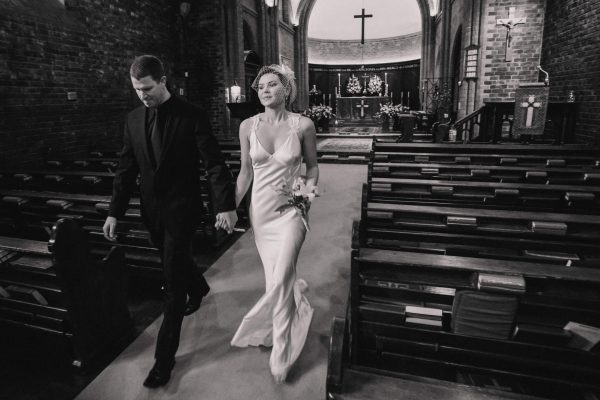 Black and white photo of the bride and groom walking out of the church to meet their guests outside.